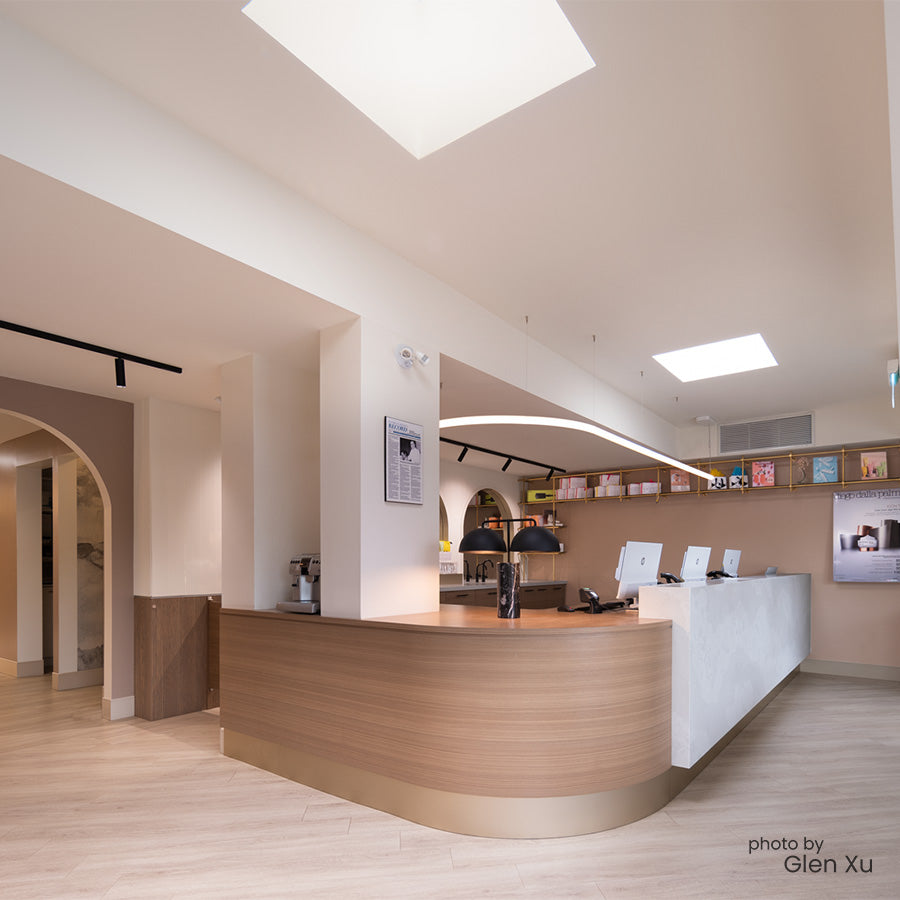 Modern spa reception area with a curved wooden desk and white walls.