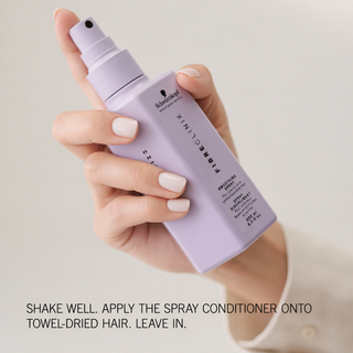Hand holding Fibre Clinix De-frizz leave-in spray bottle with instructions of how to use along the bottom.