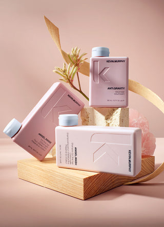 Kevin Murphy hair product bottles in pink on a wooden block with a soft pink background