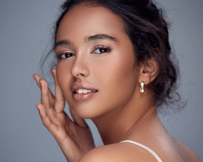 A close-up image of a person with a subtle makeup look, touching their face which indicates a lightweight application.