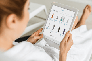 Person in white robe holding a tablet with an e-commerce app displaying product images.