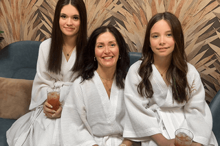 Mother and two young daughters relaxing in white robes.